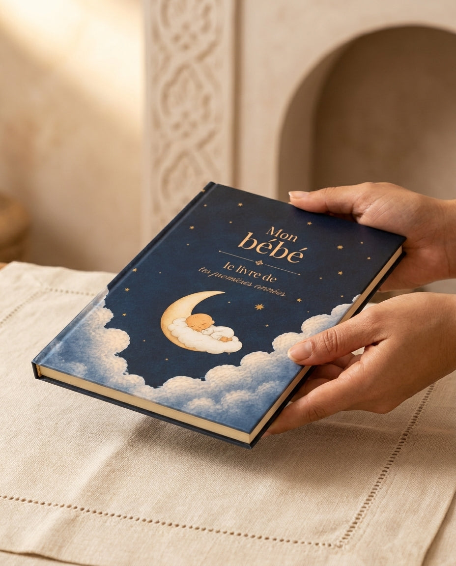 Cadeau de naissance au Maroc : mains de femme tenant le livre bébé HIKAYATAK au-dessus d'un lin beldi écru dans un intérieur marocain feutré